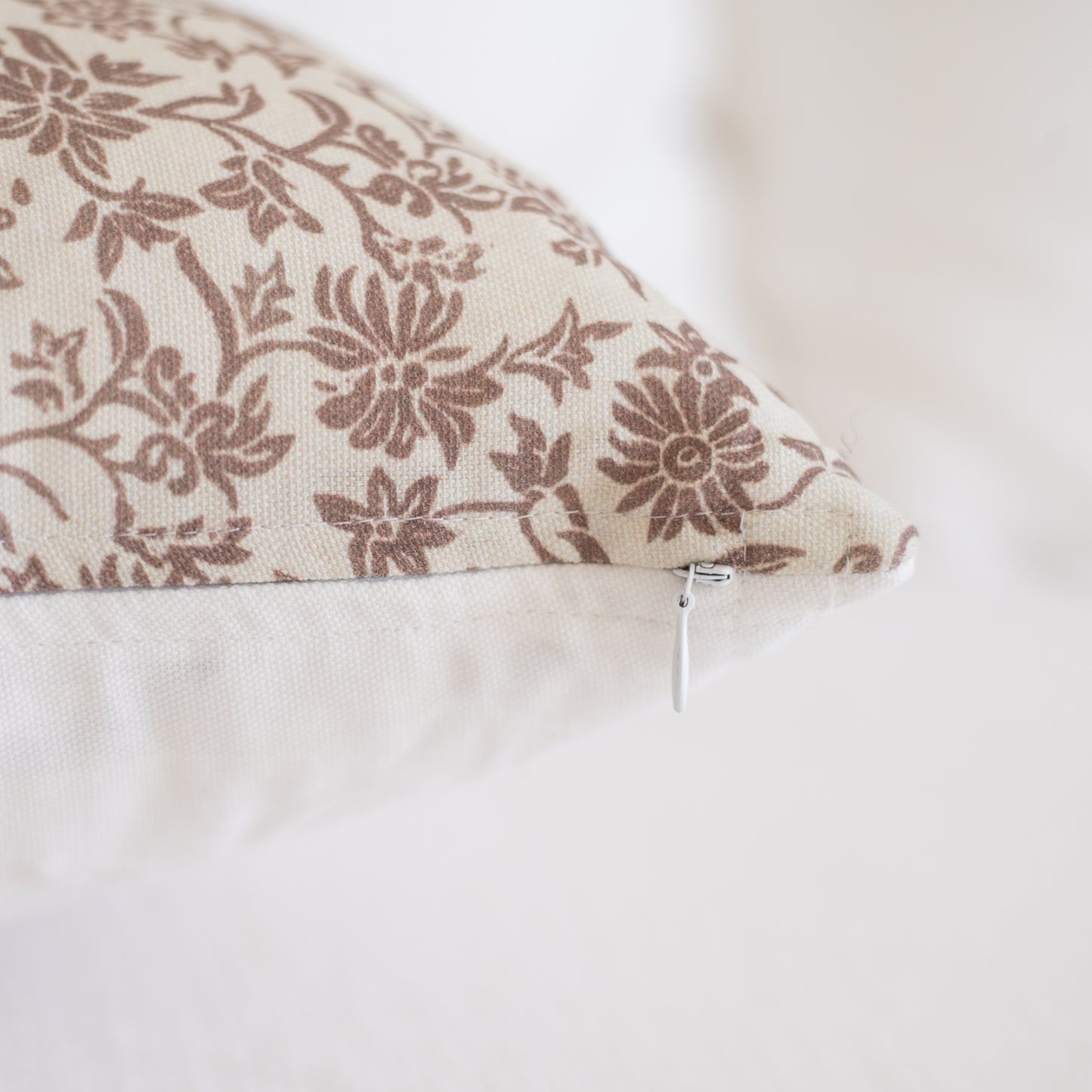 Rectangular pillow with taupe floral pattern on cream background and white zipper closure visible on side.