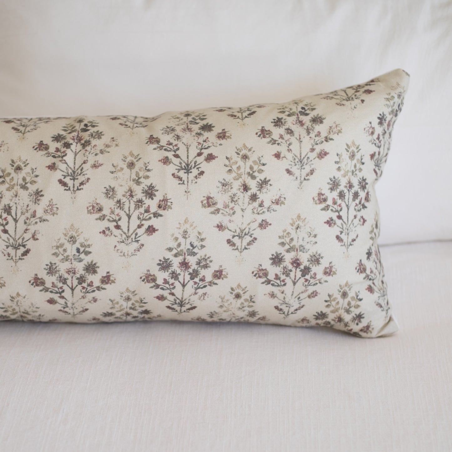 Rectangular lumbar pillow with cream linen fabric printed with small burgundy and brown botanical flowers in repeating patter