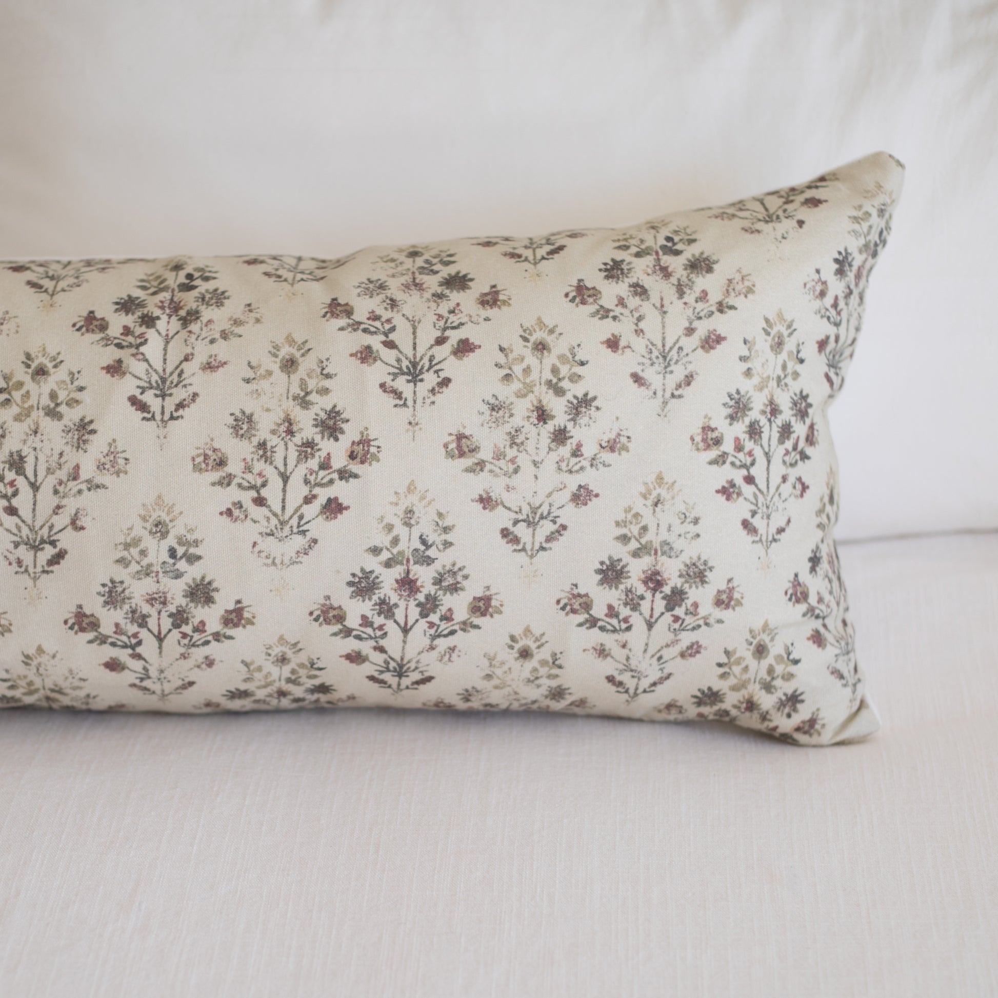 Rectangular lumbar pillow with cream linen fabric printed with small burgundy and brown botanical flowers in repeating patter