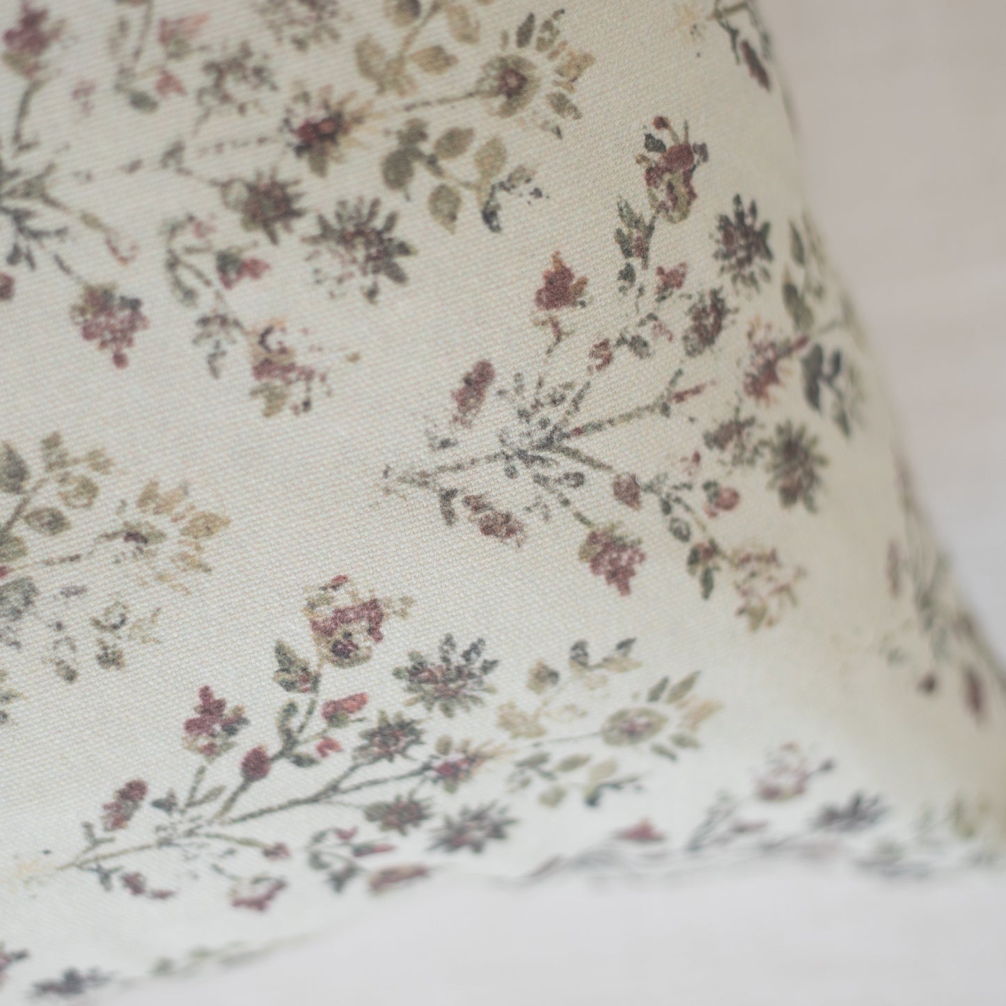 Cream-colored lumbar pillow with small burgundy and gray floral pattern throughout fabric.