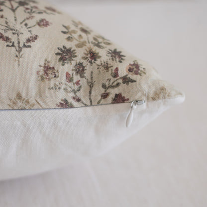 Lumbar pillow with floral botanical print in burgundy and taupe on cream fabric, white zipper visible on side.
