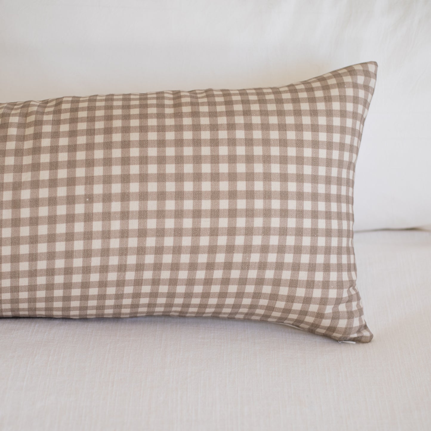 Tan and white gingham patterned lumbar pillow on white bedding.