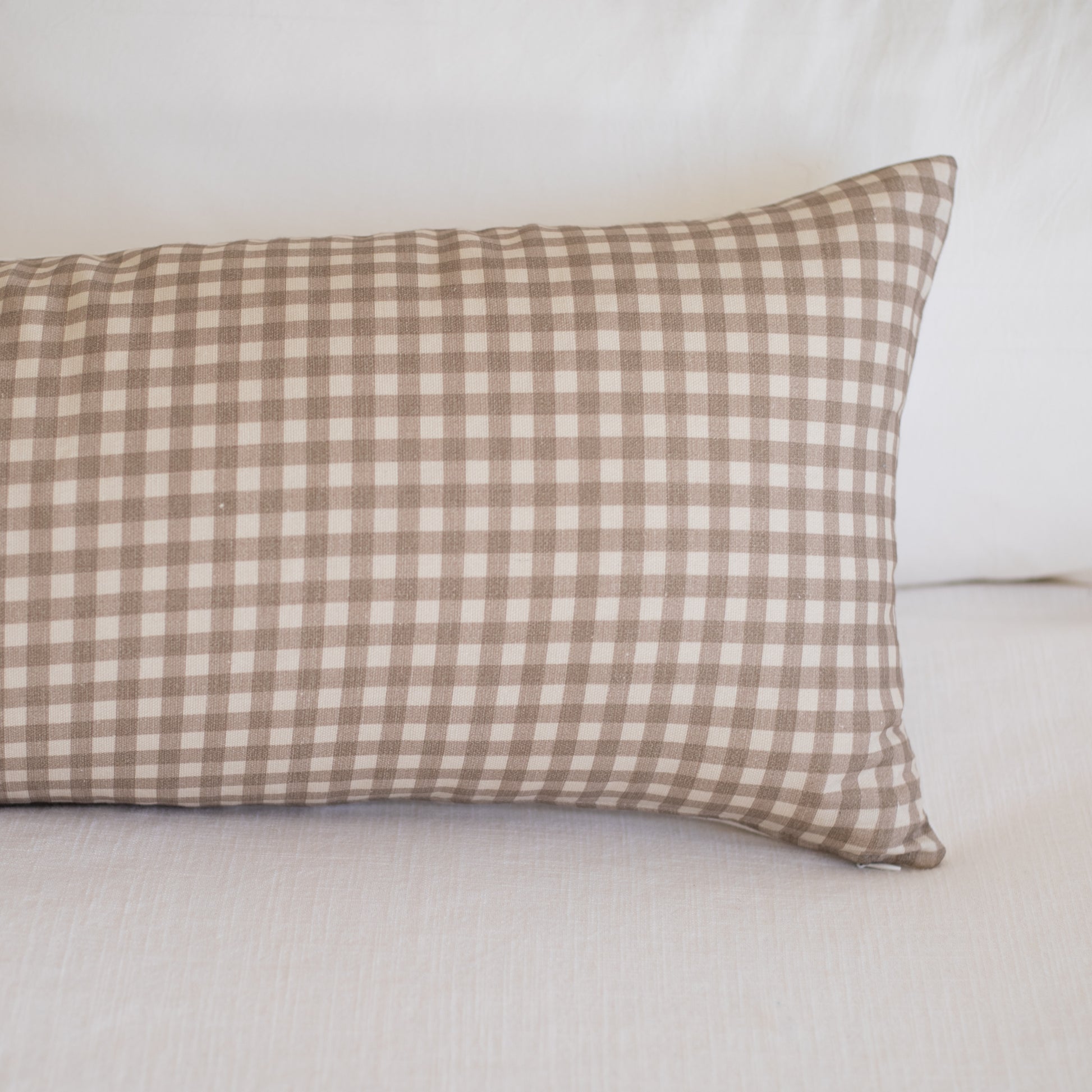 Tan and white gingham patterned lumbar pillow on white bedding.
