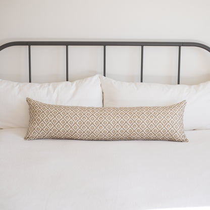 Tan and cream geometric patterned lumbar pillow on a bed with white pillows and metal headboard.
