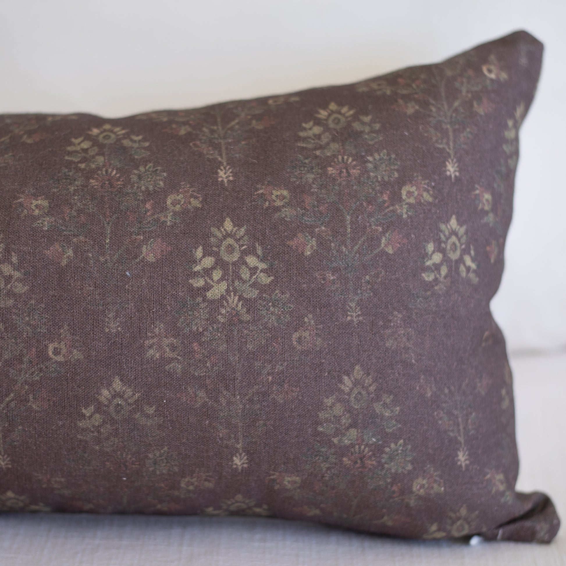 Burgundy linen pillow with small-scale floral and geometric pattern in muted gold tones.
