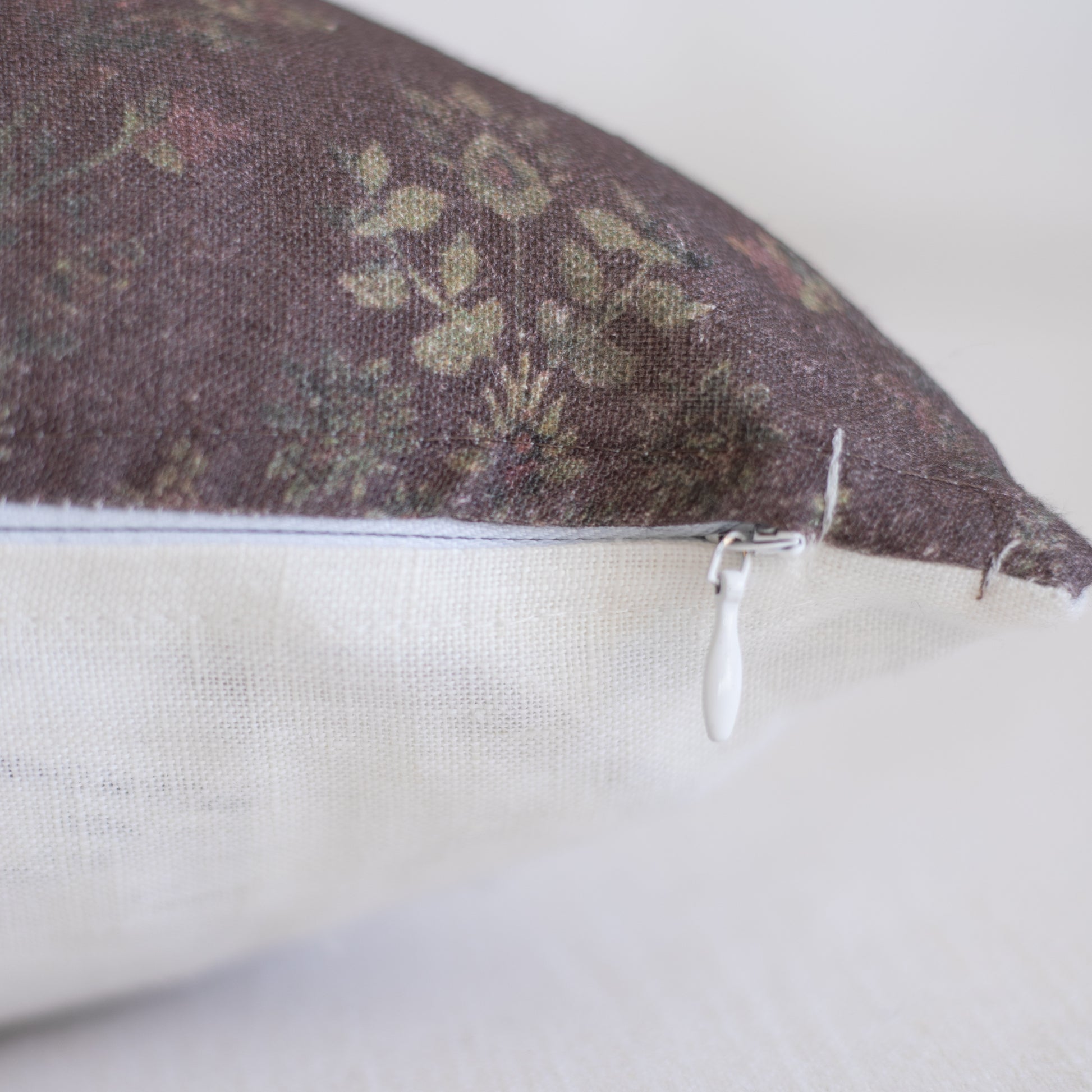 Burgundy linen pillow with muted botanical pattern and white zipper closure detail.