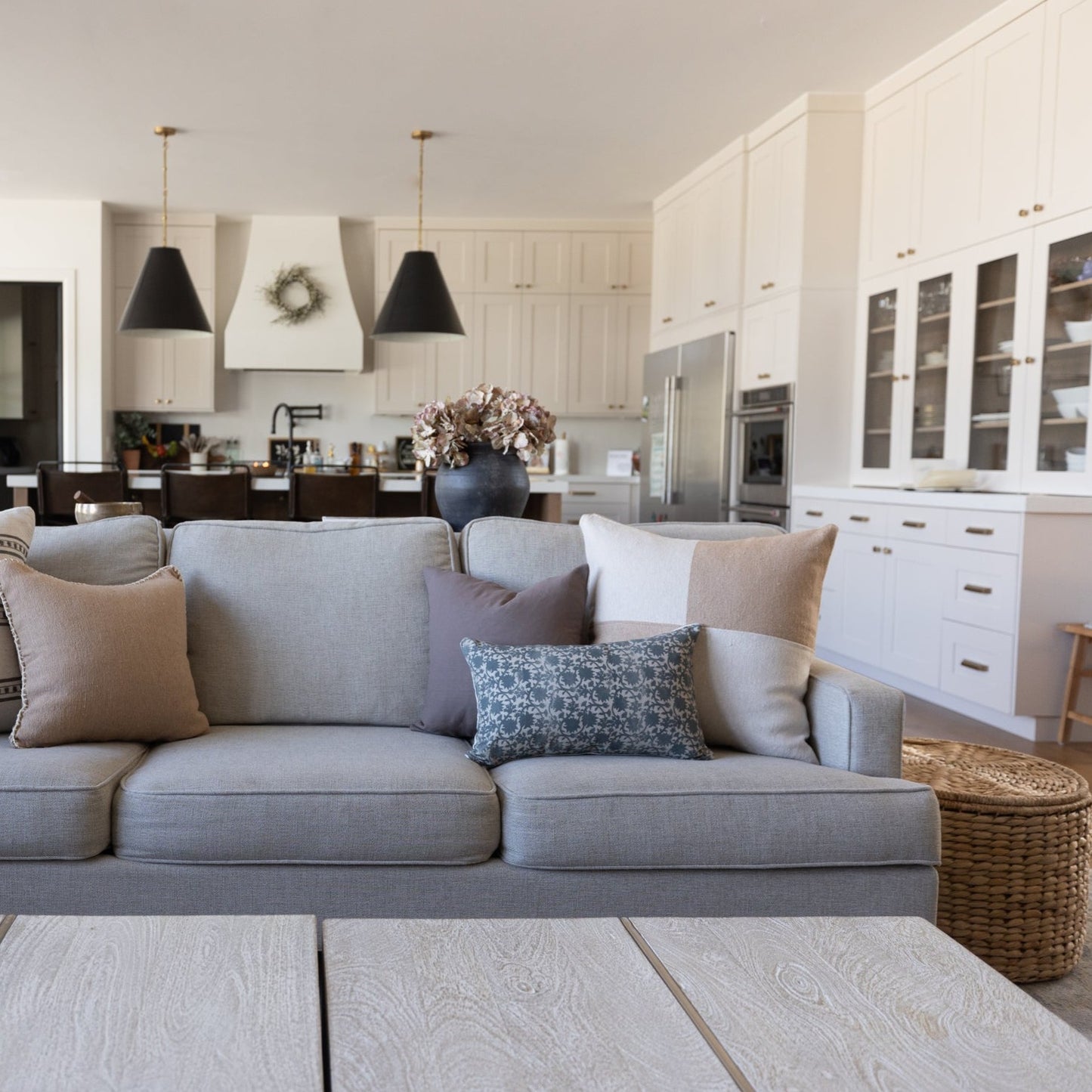 Tan and cream checkered pillow on gray upholstered sofa in open-concept living room with kitchen.