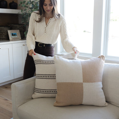 Tan and cream patchwork pillow with woven stripe detail, displayed on a light beige sofa.