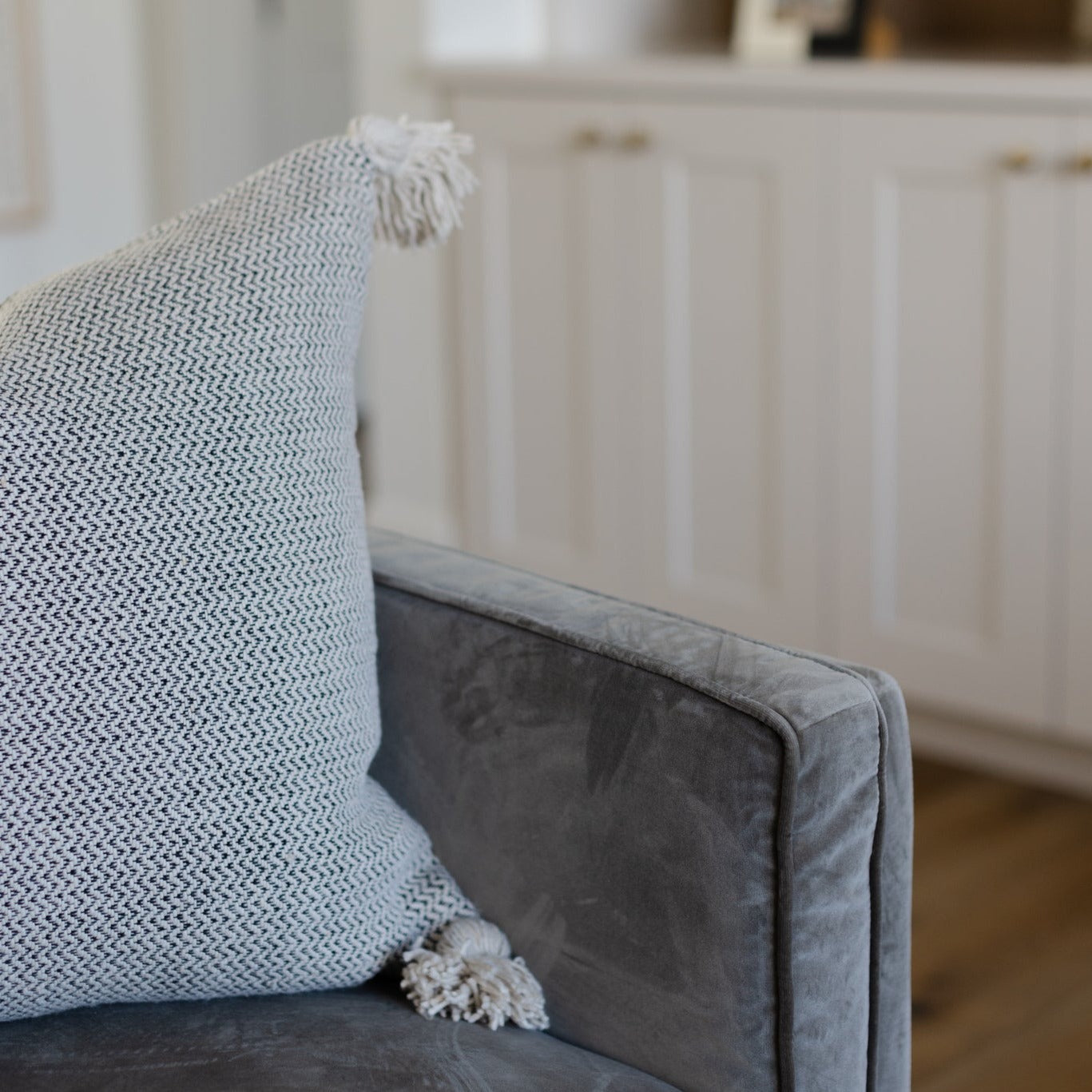 Cream tweed pillow with textured weave and fringe tassel detail on gray upholstered chair.