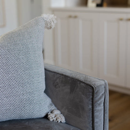 Cream tweed pillow with textured weave and fringe tassel detail on gray upholstered chair.