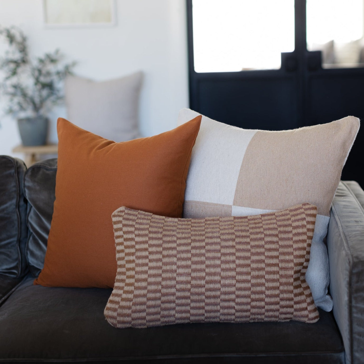 Tan and white checkered lumbar pillow displayed on a sofa with solid and patterned accent pillows.