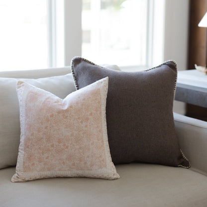 Two decorative pillows on a light sofa: one beige with damask pattern, one charcoal gray with nailhead trim.