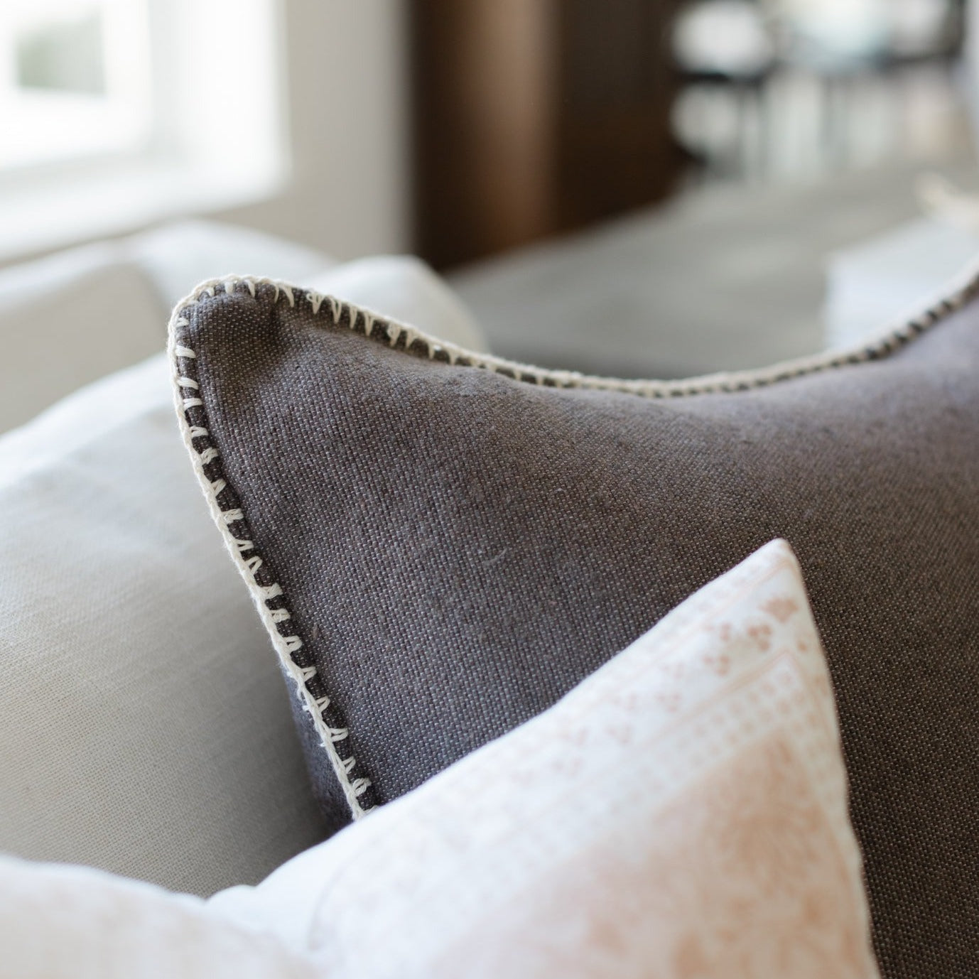 Charcoal gray throw pillow with whipstitched edges, displayed on a sofa.