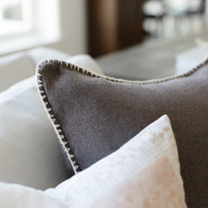 Charcoal gray throw pillow with whipstitched edges, displayed on a sofa.