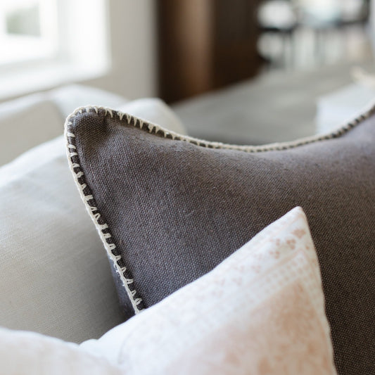 Charcoal gray throw pillow with whipstitched edges, displayed on a sofa.