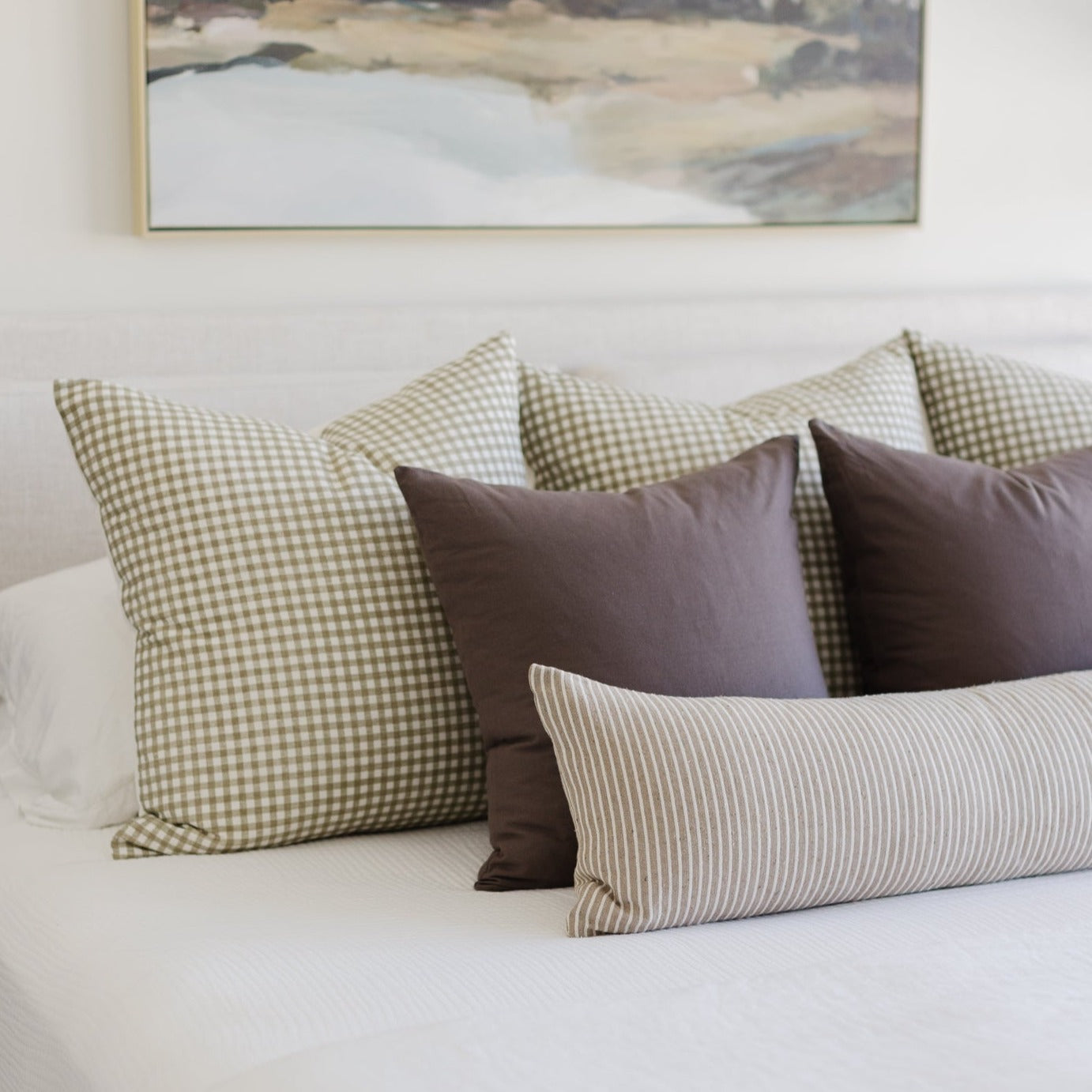Decorative pillows in mocha, sage gingham, and striped patterns arranged on a bed.