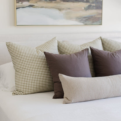 Decorative pillows in mocha, sage gingham, and striped patterns arranged on a bed.
