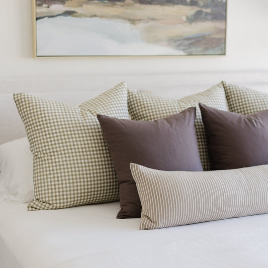 Decorative pillows in mocha, sage gingham, and striped patterns arranged on a bed.