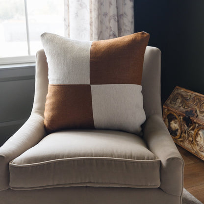 Square pillow with brown and cream checkered pattern on beige upholstered chair by window.