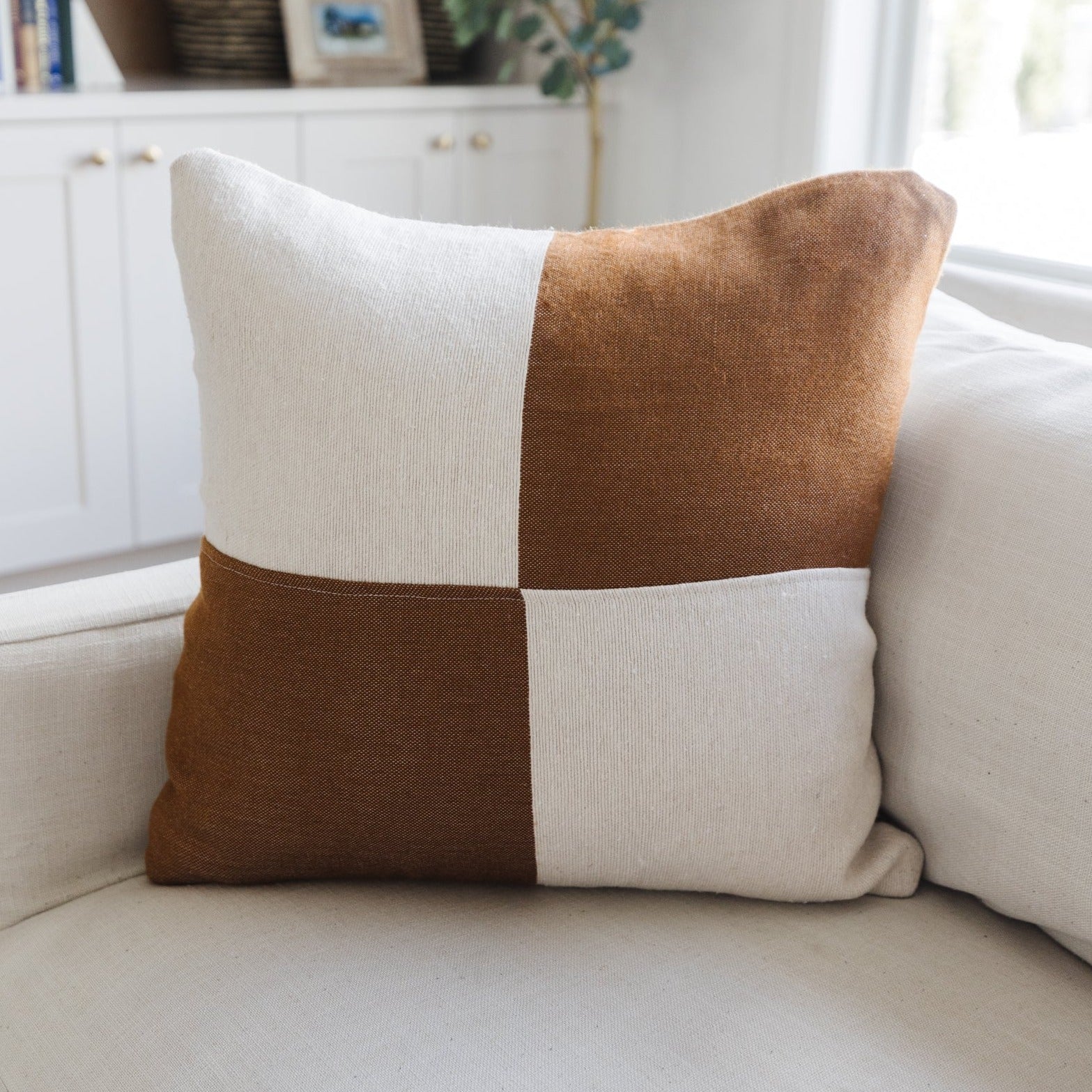 Brown and cream checkered throw pillow with four-block pattern displayed on a beige sofa.