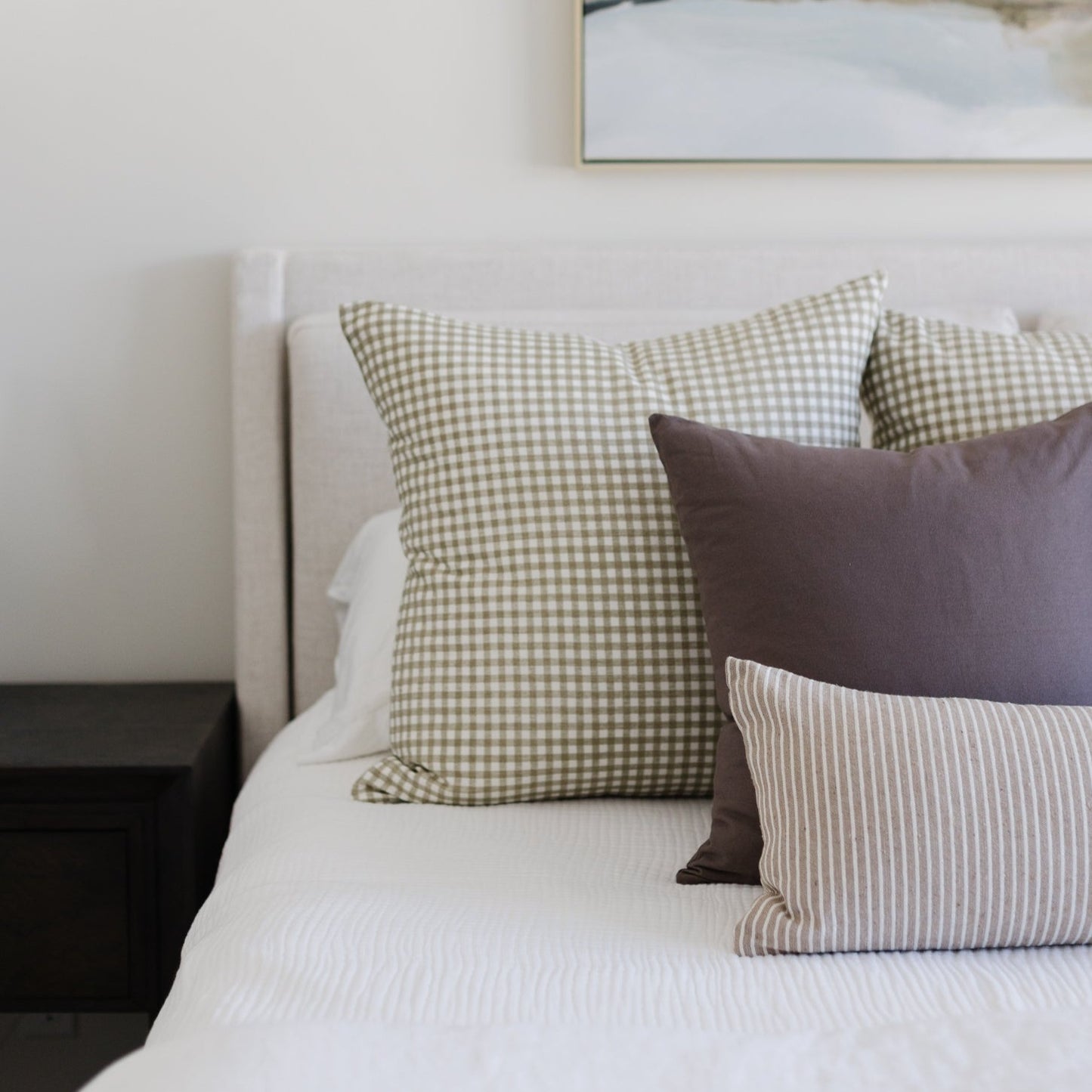 Gingham checkered pillow in sage and white displayed on a bed with solid and striped pillows.