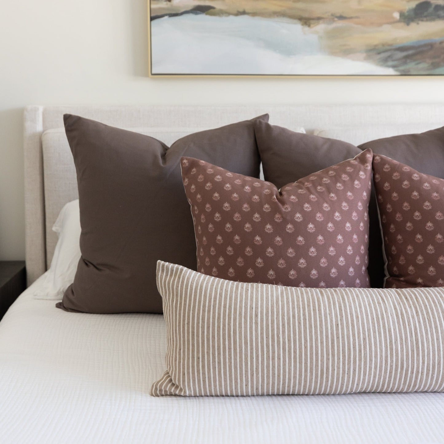 Brown and beige pillows arranged on a bed, including solid brown, patterned damask, and striped designs.
