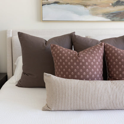Brown and beige pillows arranged on a bed, including solid brown, patterned damask, and striped designs.