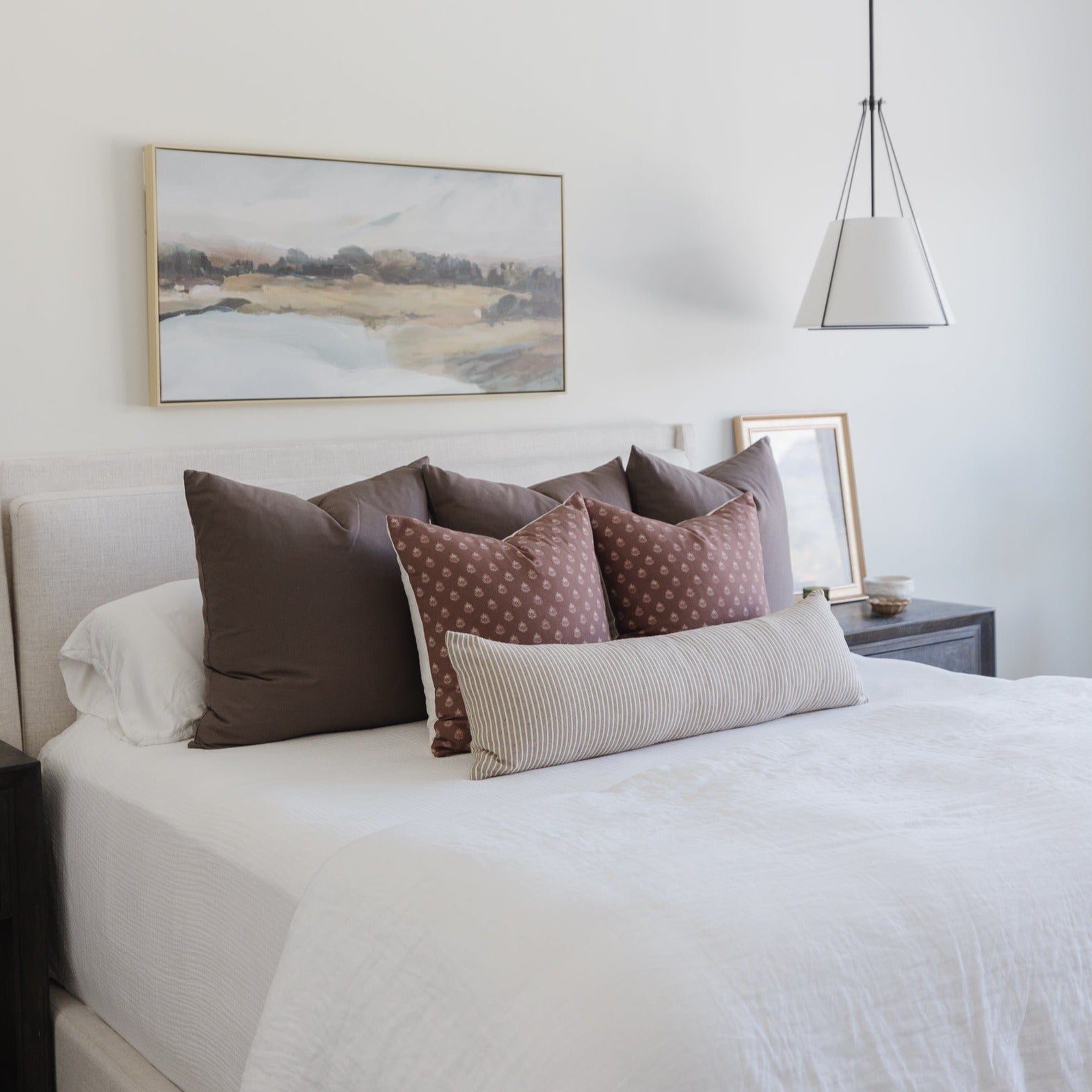 Mocha-colored pillows arranged on a bed with white bedding, including solid and patterned cushions in various sizes.