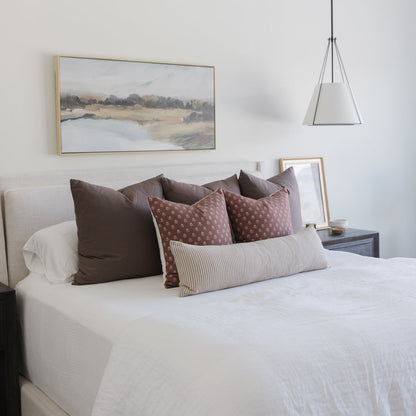 Mocha-colored pillows arranged on a bed with white bedding, including solid and patterned cushions in various sizes.