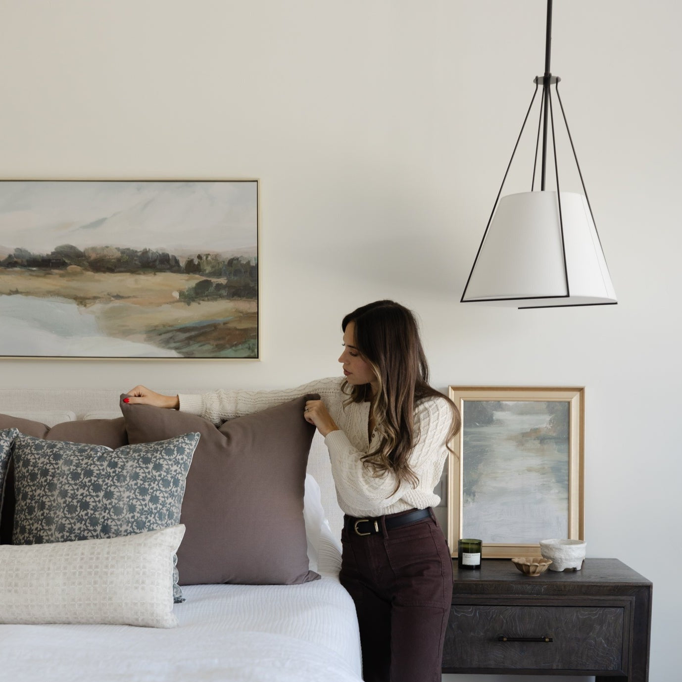 Tapered pendant light with white fabric shade and black metal frame hanging above bedroom nightstand.