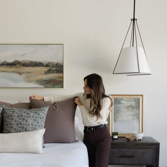 Tapered pendant light with white fabric shade and black metal frame hanging above bedroom nightstand.