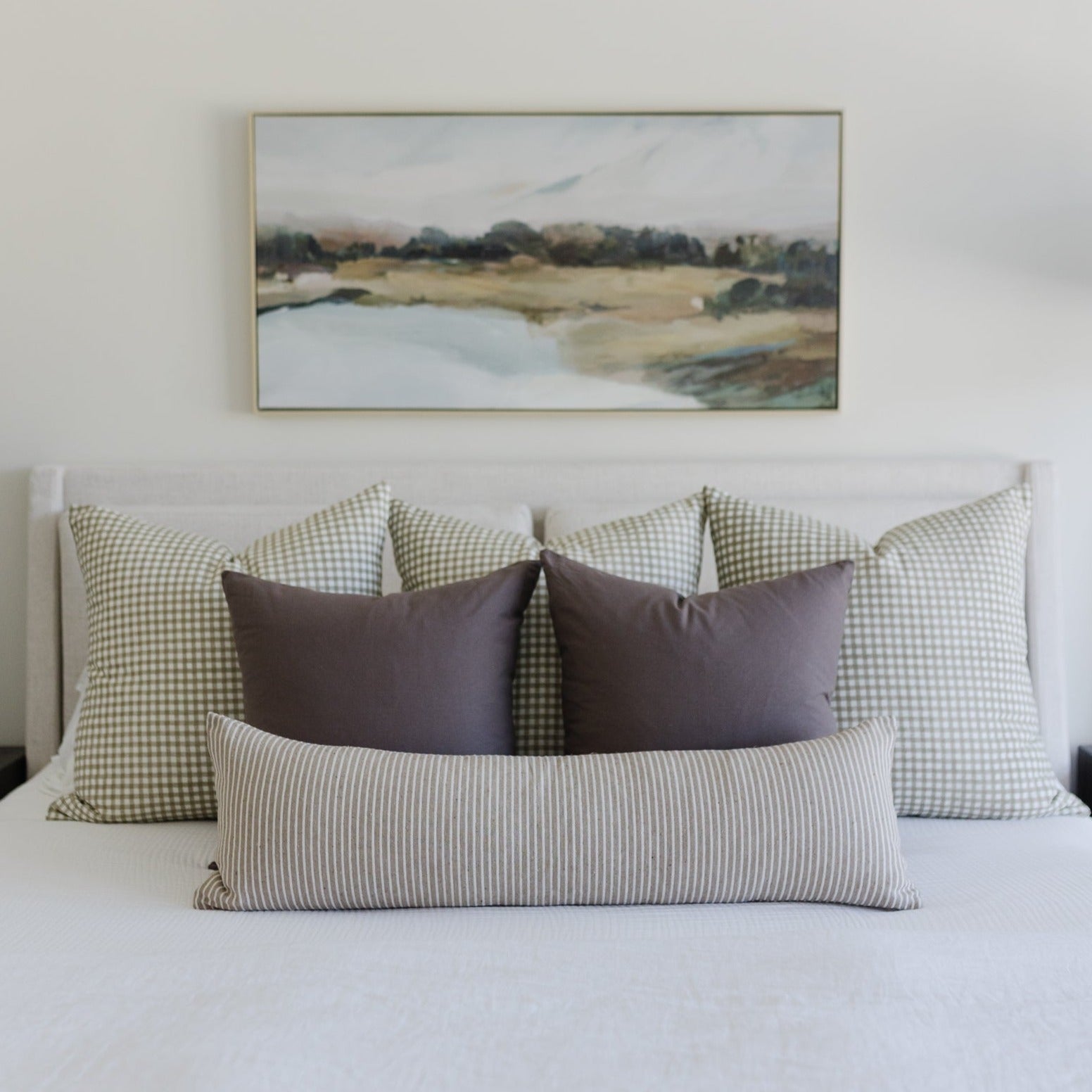 Bed styled with green and white checkered pillows, striped lumbar pillow, and solid mocha pillows arranged against white head