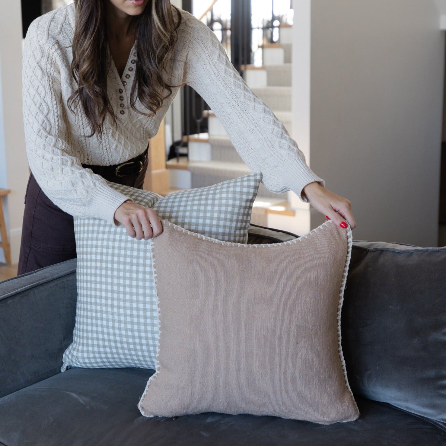 Gingham patterned pillow in light blue and white with beige textured back displayed on dark sofa.