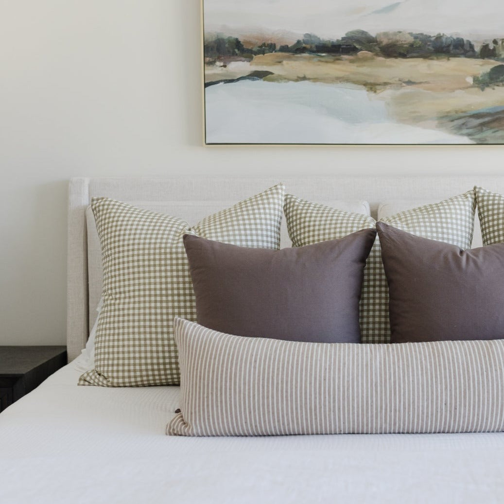 Gingham patterned throw pillow in sage green and white gingham check displayed on bed with coordinating striped pillow.