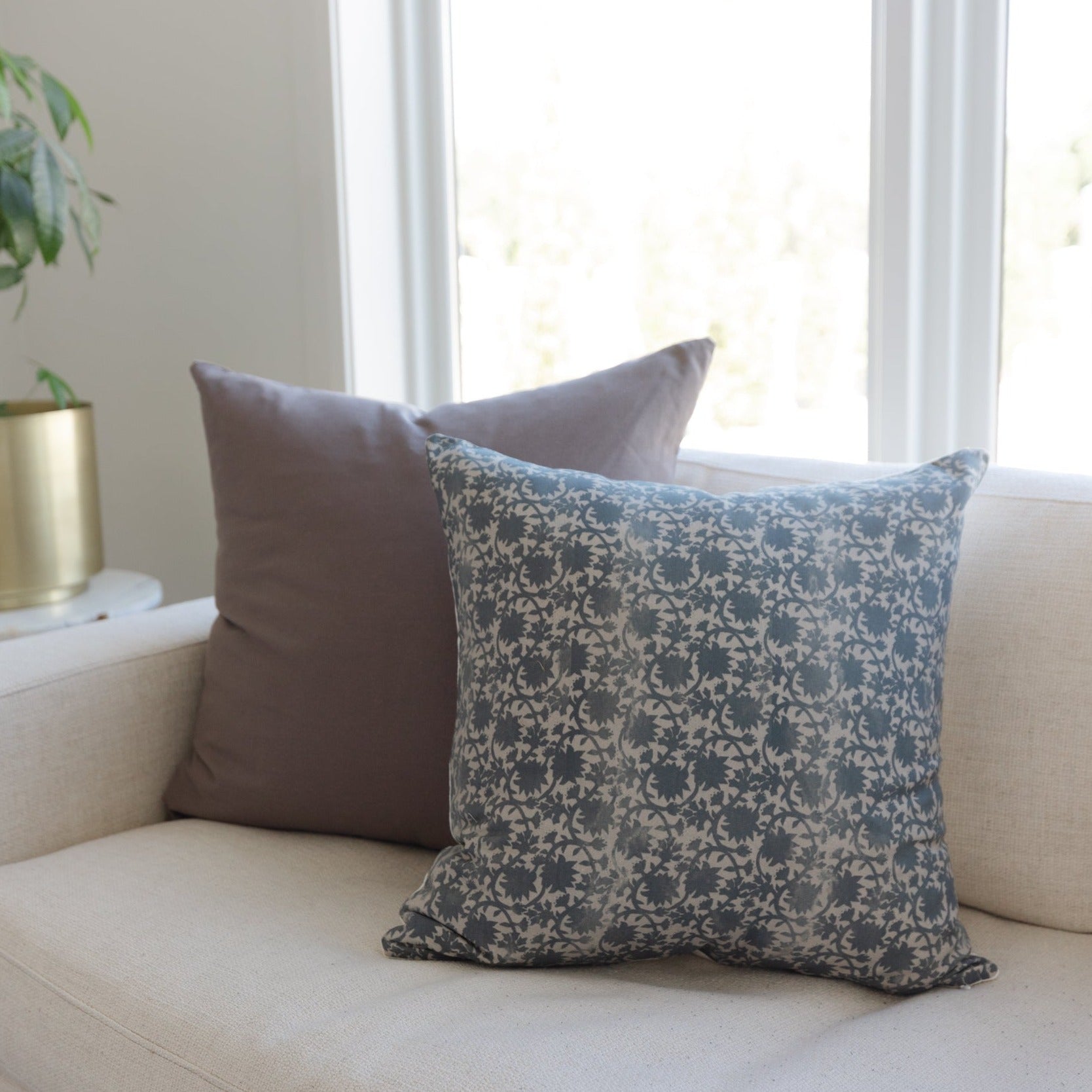 Two decorative pillows on a cream sofa: one solid gray and one with blue damask pattern.