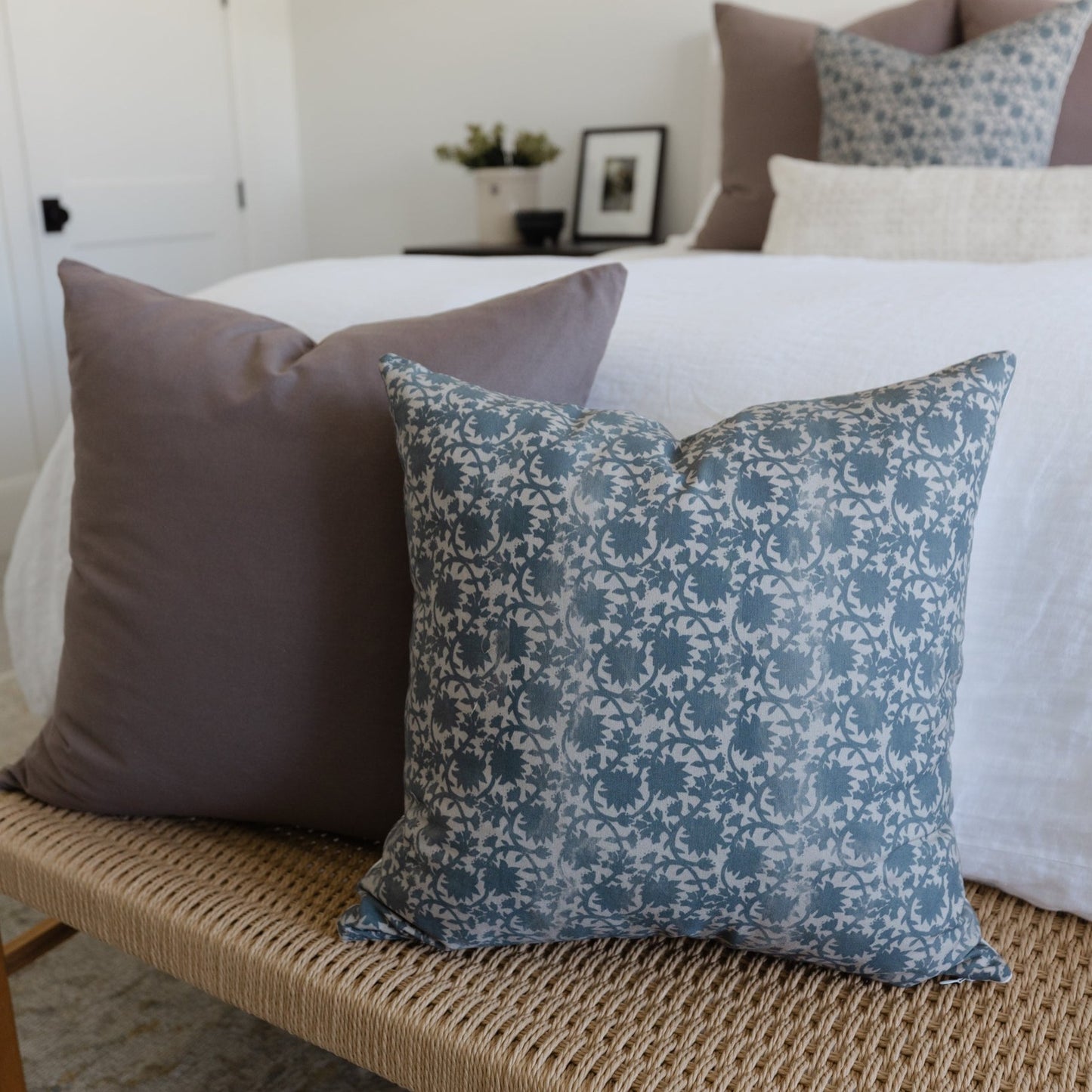 Blue damask patterned throw pillow displayed on a bed with solid taupe pillow and white bedding.
