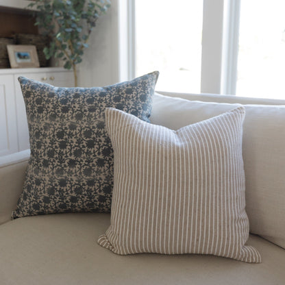 Two decorative pillows on a cream-colored sofa: one with blue damask pattern, one with tan and white vertical stripes.