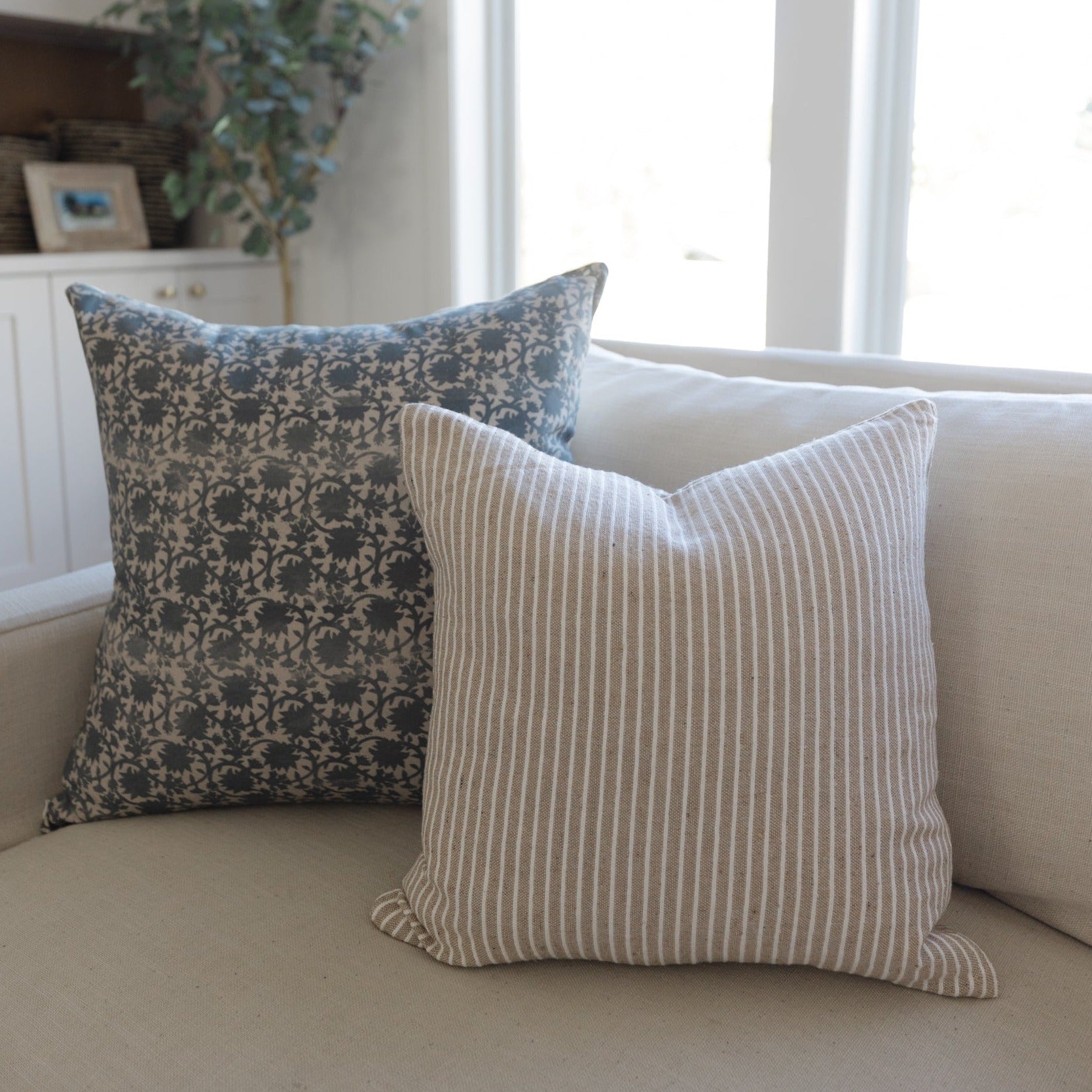Two decorative pillows on a tan sofa: one with blue damask pattern, one with tan and white vertical stripes.