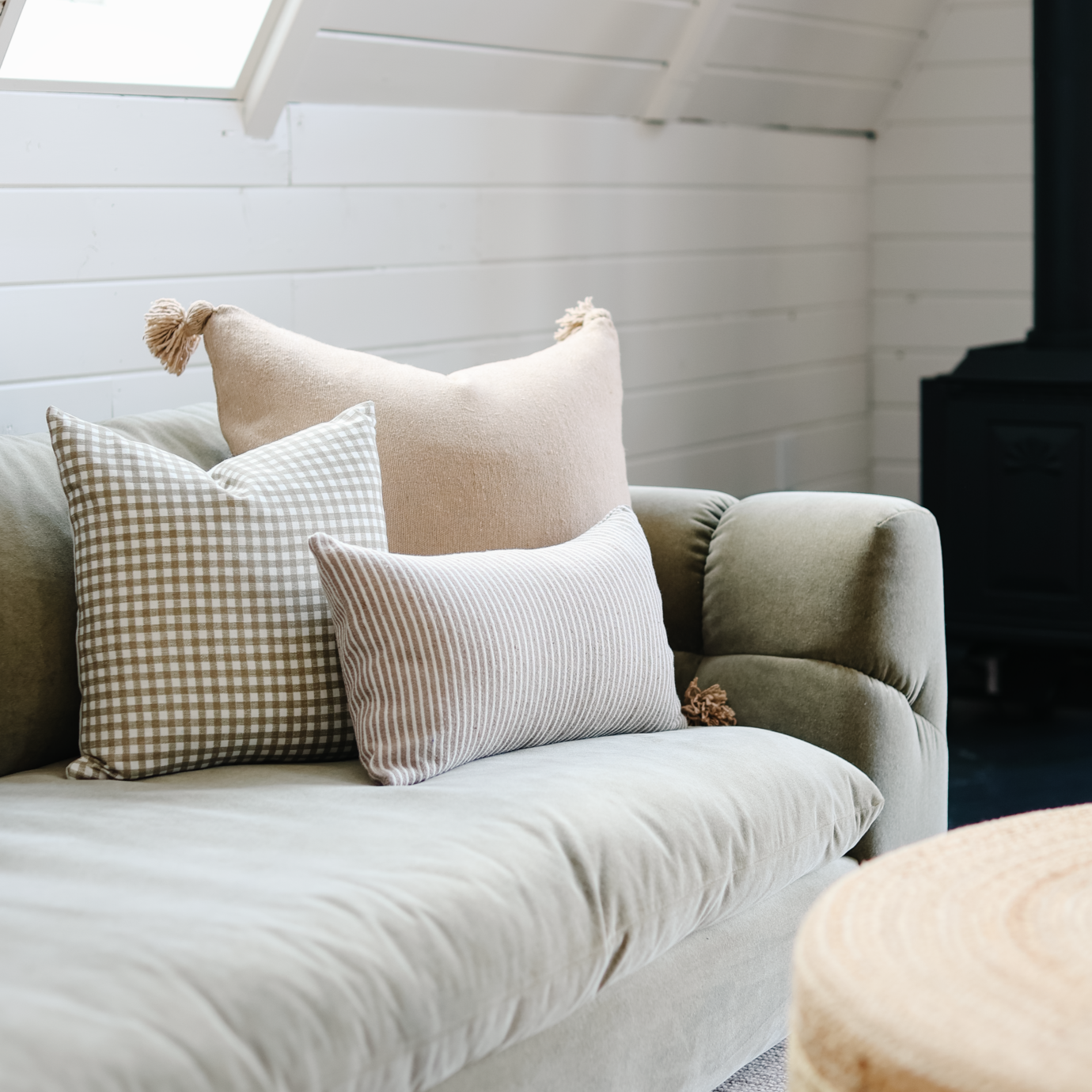Tan lumbar pillow with tassel displayed on a sofa with gingham and striped accent pillows.