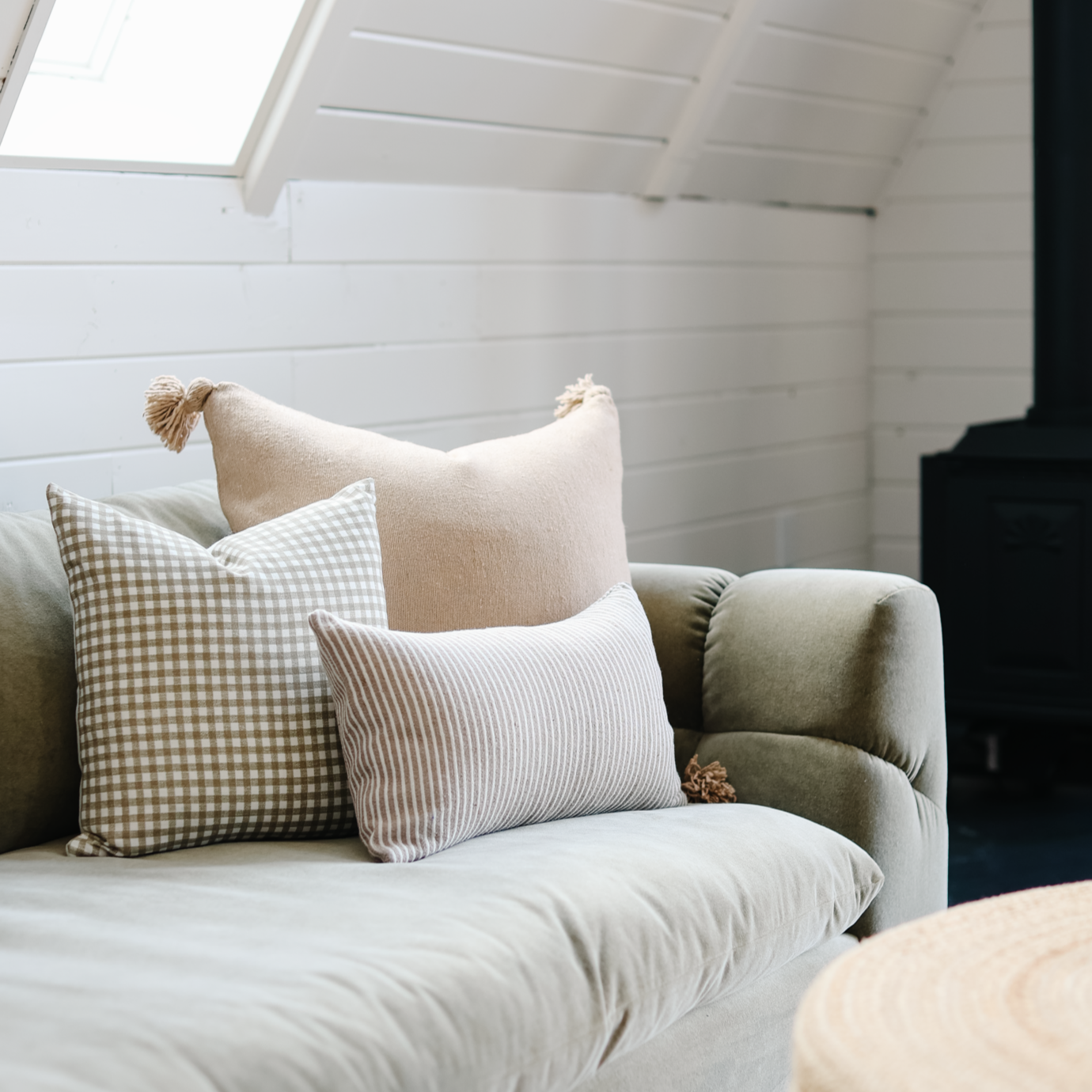 Cream wool pillow with tassel displayed on upholstered chair with patterned throw pillows in bright room.