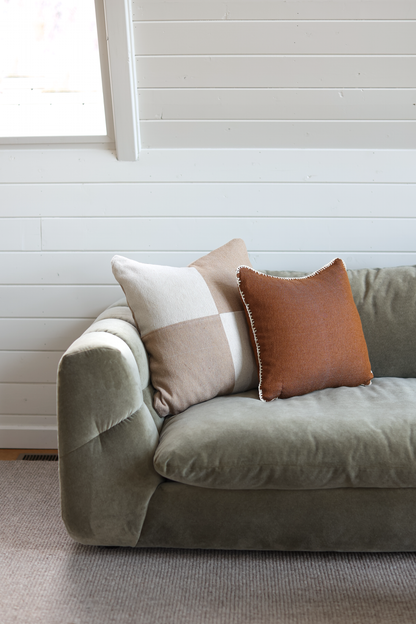 Beige and rust linen pillows with checkered and solid patterns arranged on a light green upholstered sofa.