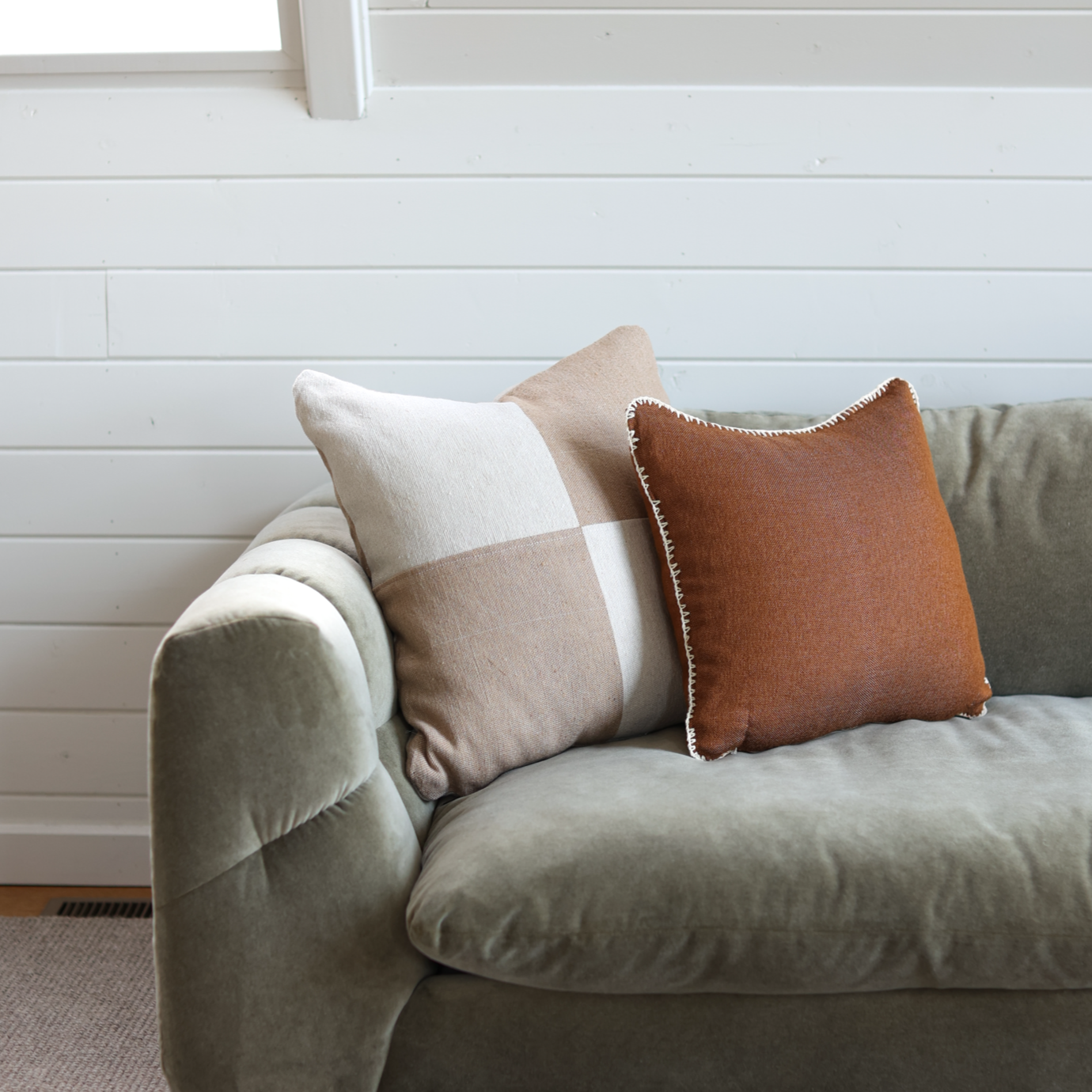 Rust-colored throw pillow with whipstitched edges displayed on a gray sofa with coordinating neutral pillows.