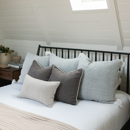 Tan lumbar pillow with textured fabric and decorative stitching displayed on a bed with coordinating pillows.