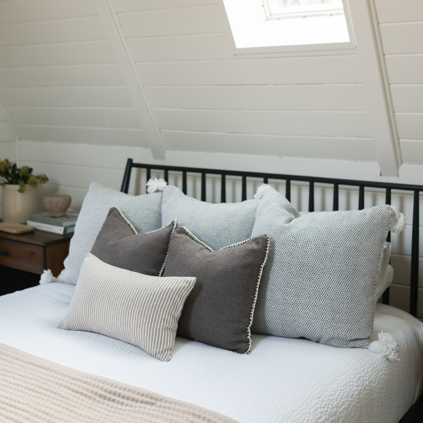 Tweed cushion in gray with white piping, displayed on bed with coordinating pillows in neutral tones.