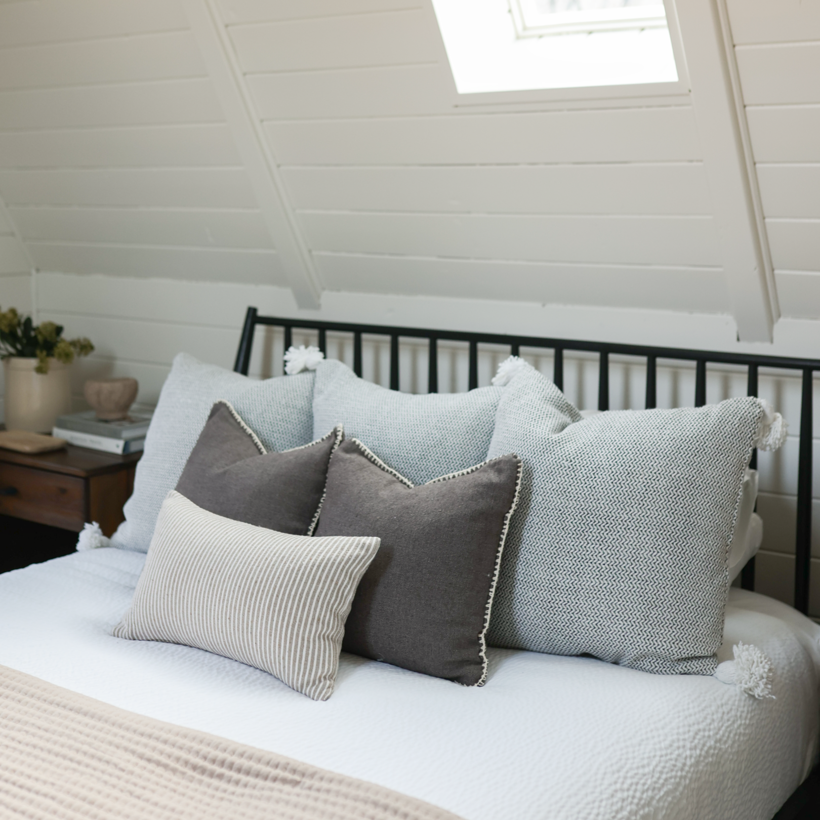 Tweed cushion in gray with white piping, displayed on bed with coordinating pillows in neutral tones.