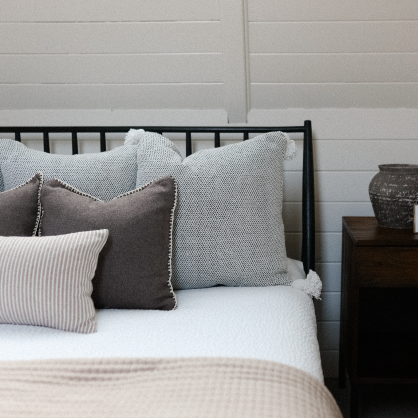 Warm charcoal throw pillow with nailhead trim displayed on bed with other decorative pillows.