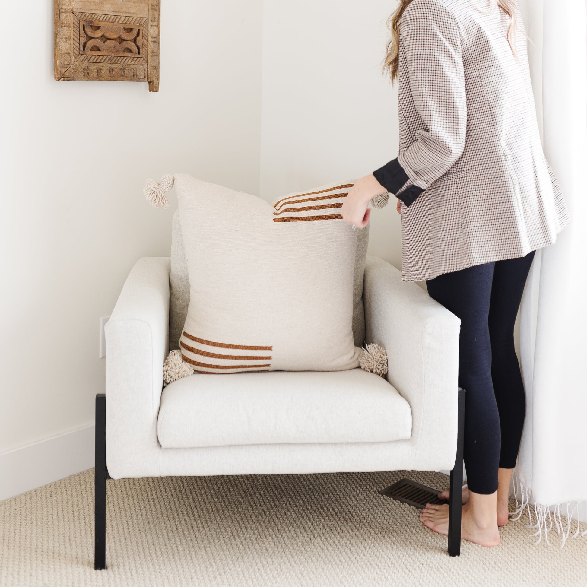 Cream-colored upholstered armchair with black metal legs and rust striped throw pillow.