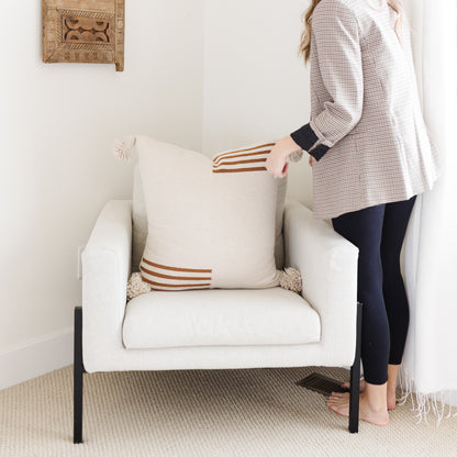 Cream-colored upholstered armchair with black metal legs and rust striped throw pillow.