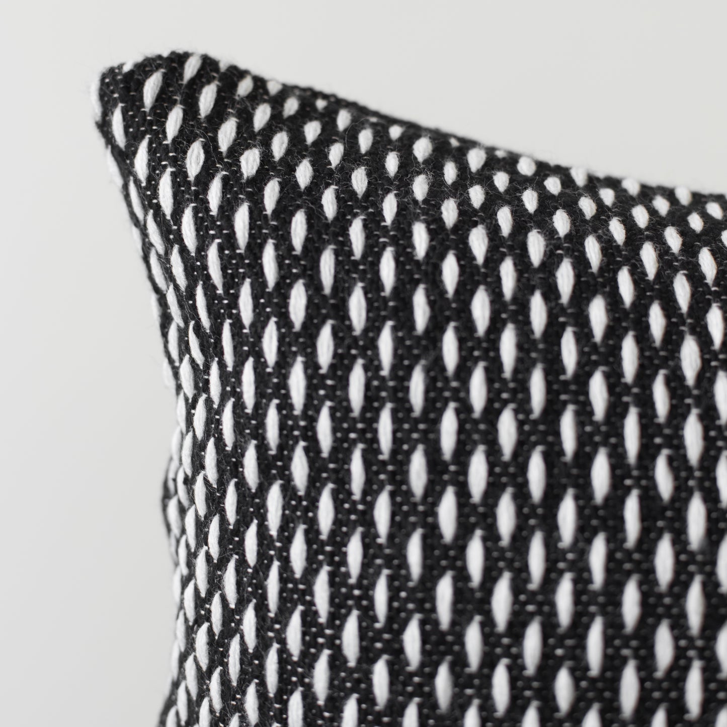 Black and white open-weave lumbar pillow with repeating oval cutout pattern and visible corner edge detail.