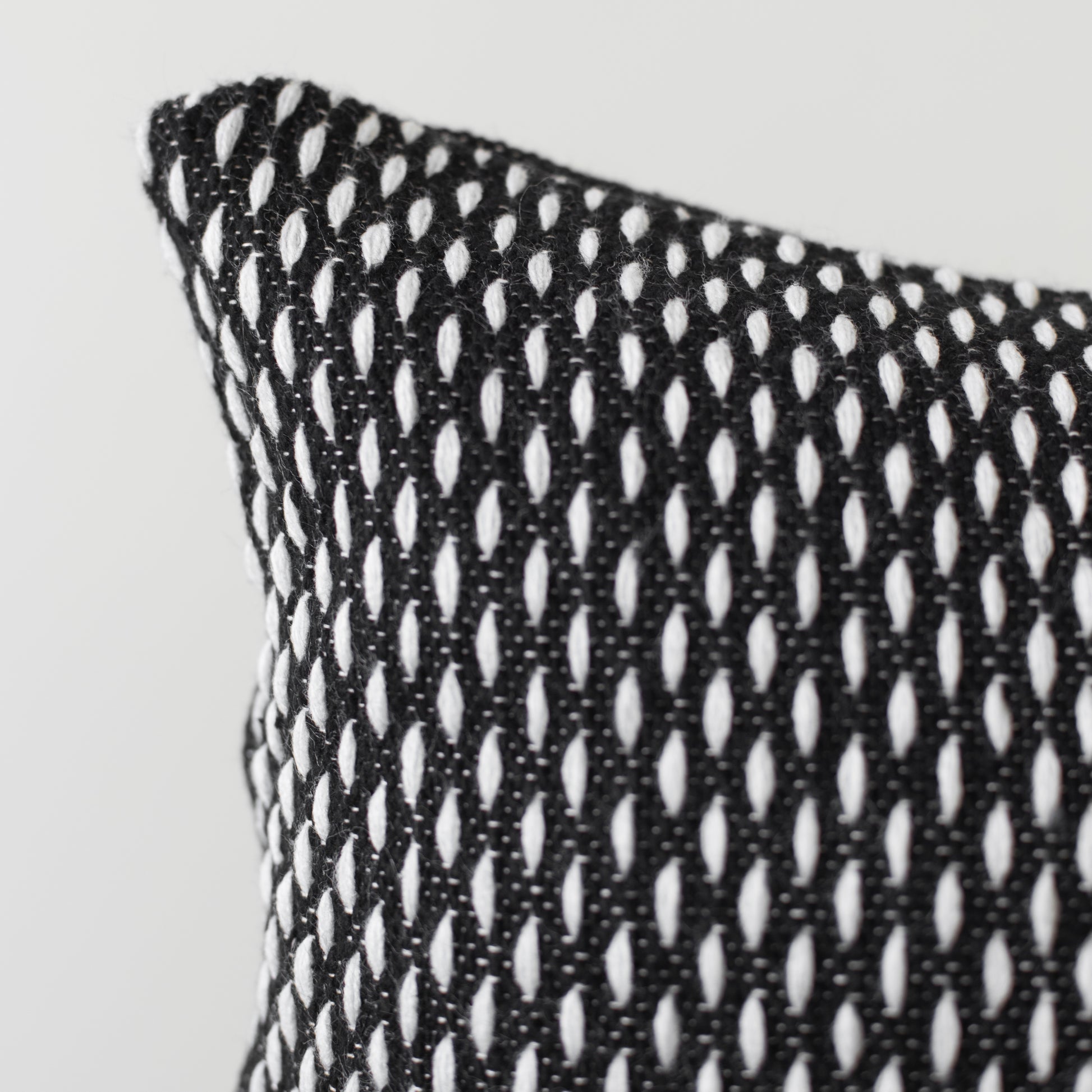 Black and white open-weave lumbar pillow with repeating oval cutout pattern and visible corner edge detail.